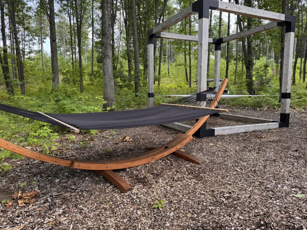A wooden hammock and pergola seating area in the forest at Glen Oro Farm, part of the guest lounge space near the fire pit