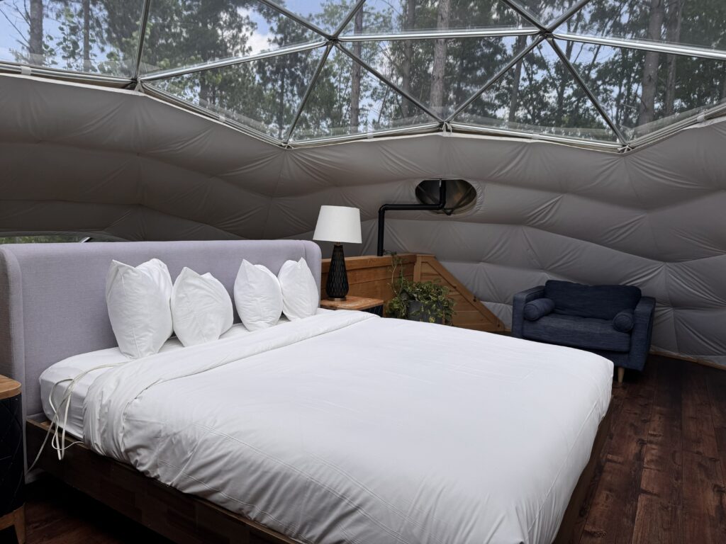Interior of a glamping dome bedroom at Glen Oro Farm with a queen bed, side table, and lounge chair