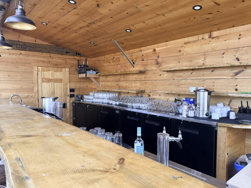 Wooden bar and beverage station inside a barn-style building at Glen Oro Farm, set up with glassware and drink dispensers