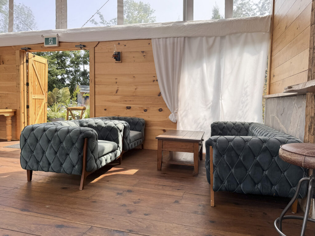 Covered lounge seating area at Glen Oro Farm with velvet sofas, a wood side table, and an open barn door overlooking the garden