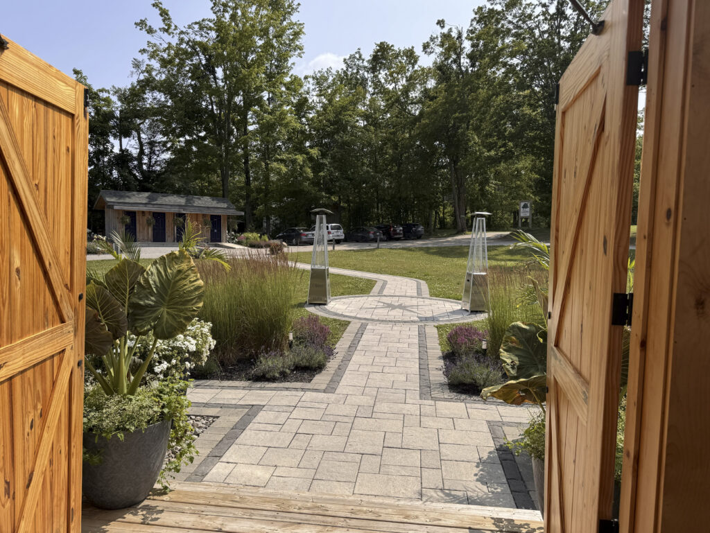 View through open barn doors onto a stone pathway and landscaped garden at Glen Oro Farm, with the parking area visible beyond