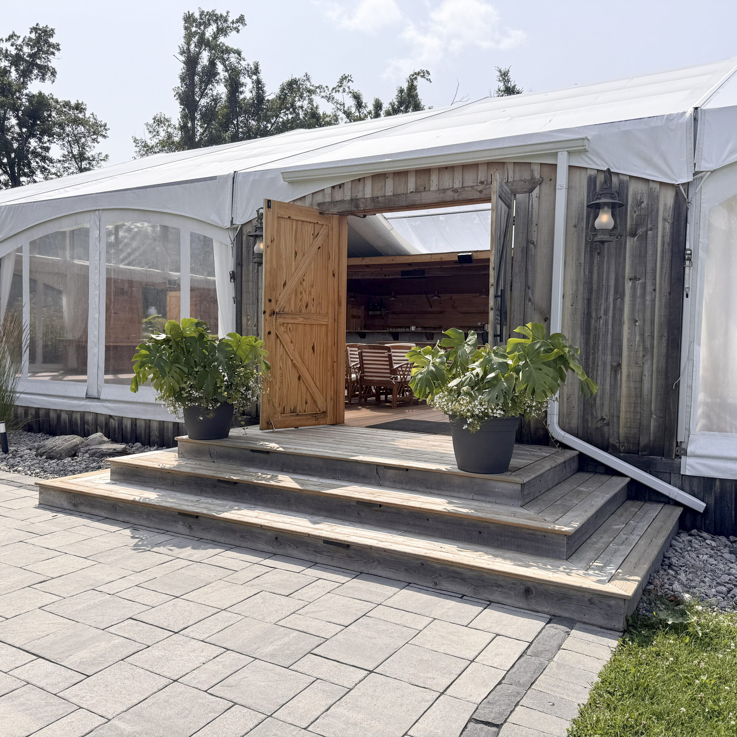 Rustic wood and glass tent exterior with stone patio and potted plants at Glen Oro Farm, Oro-Medonte, Ontario