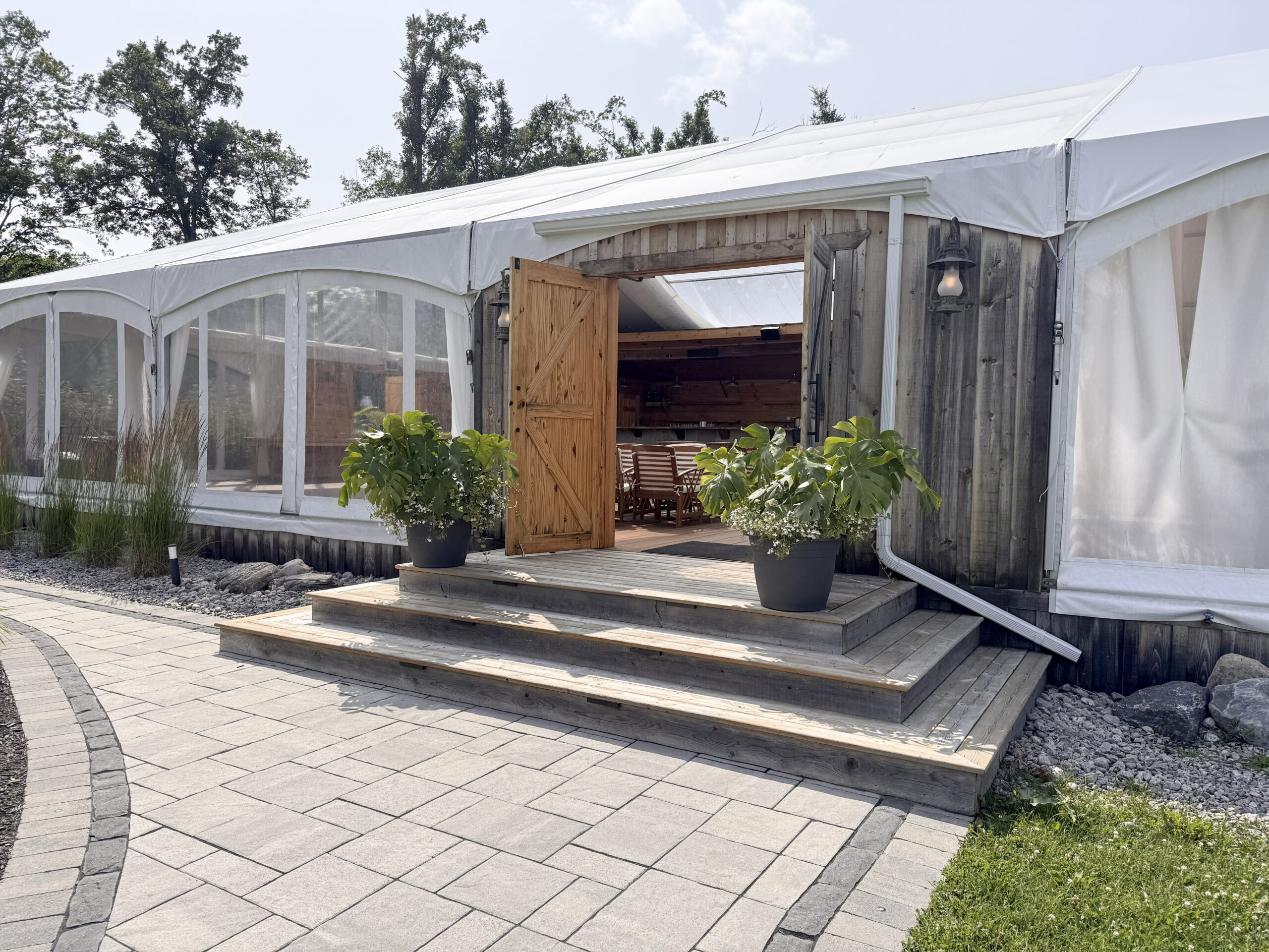 Exterior entrance of Glen Oro Farm's tented event space with wooden barn doors and stone patio pathway, Bala Muskoka wedding venue