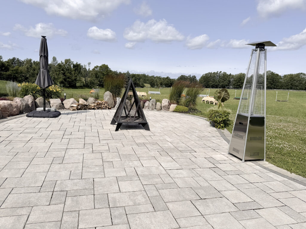 Stone patio at Glen Oro Farm with a fire feature, patio heater, and umbrella overlooking the horse jump field