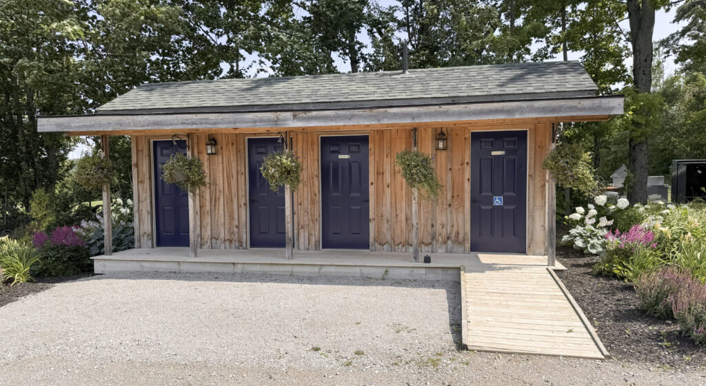 Wooden washroom building at Glen Oro Farm with multiple stalls, hanging flower baskets, and a wheelchair-accessible ramp