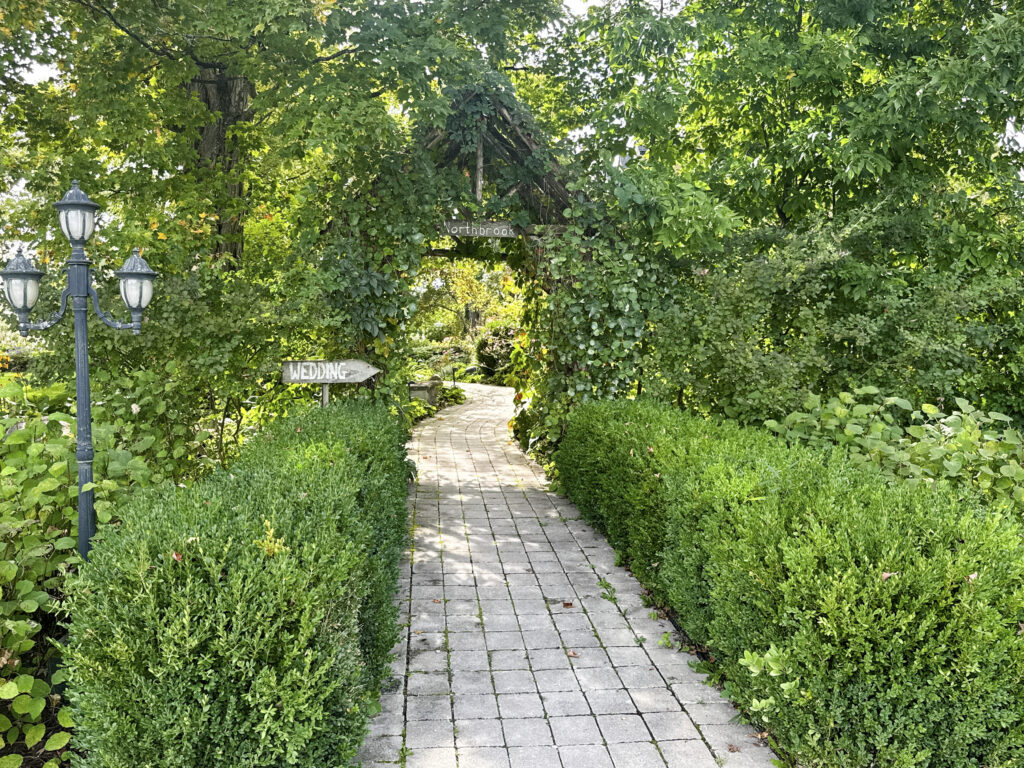 Brick paver pathway leading through a green garden arbor at Northbrook Farm
