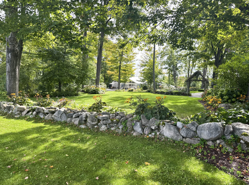 Sunny lawn with a stone wall and mature trees at Northbrook Farm wedding venue