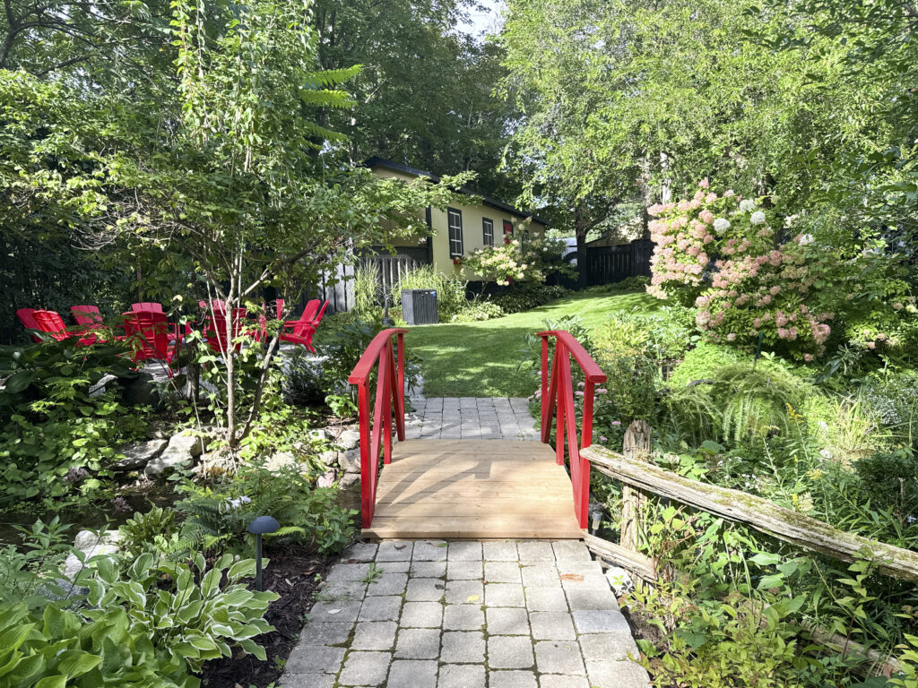 Red wooden footbridge over a stone path with blooming flowers at Northbrook Farm