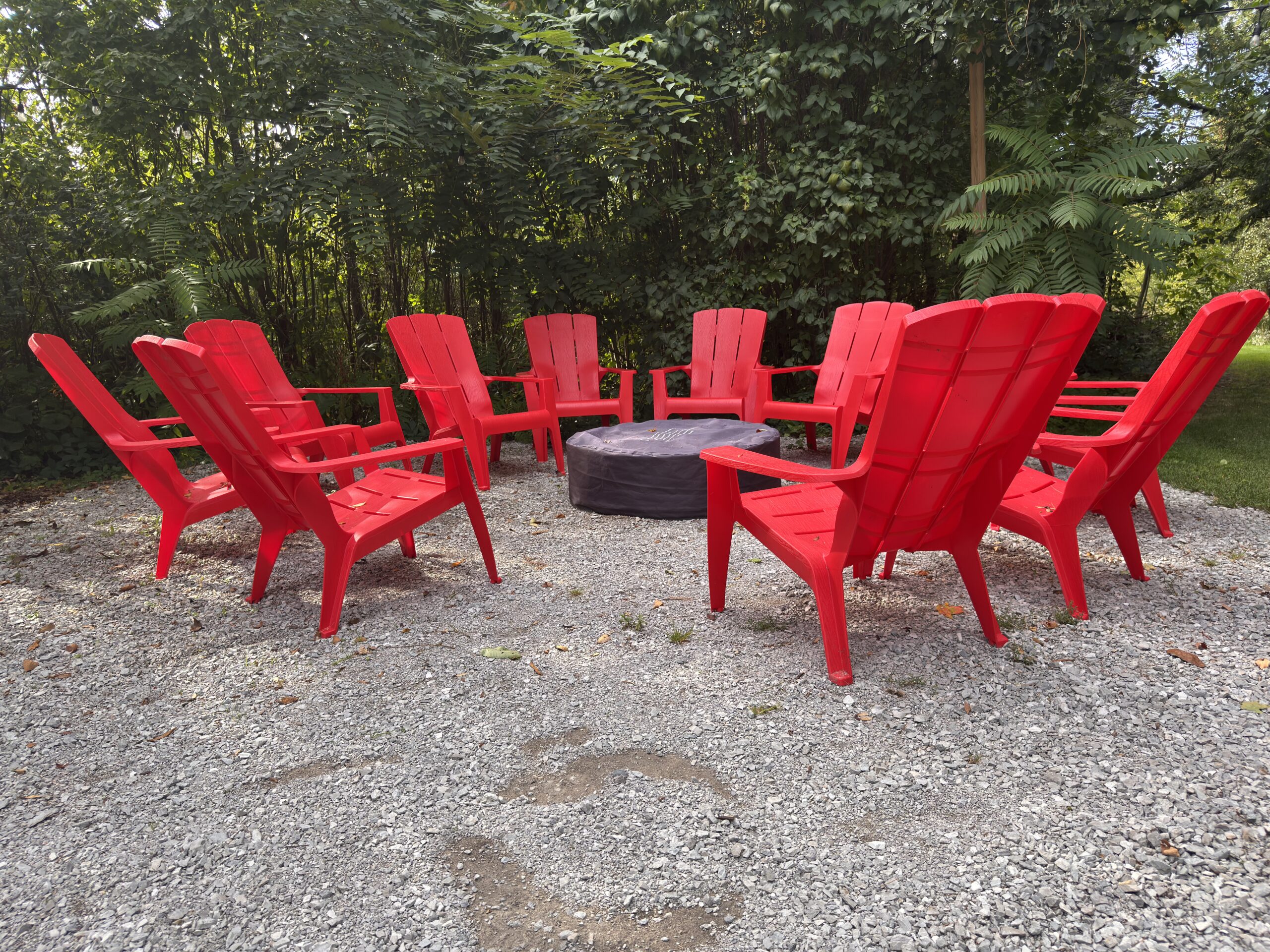 Circle of red Adirondack chairs around a stone fire pit on a gravel patio at Northbrook Farm near Orillia, Ontario