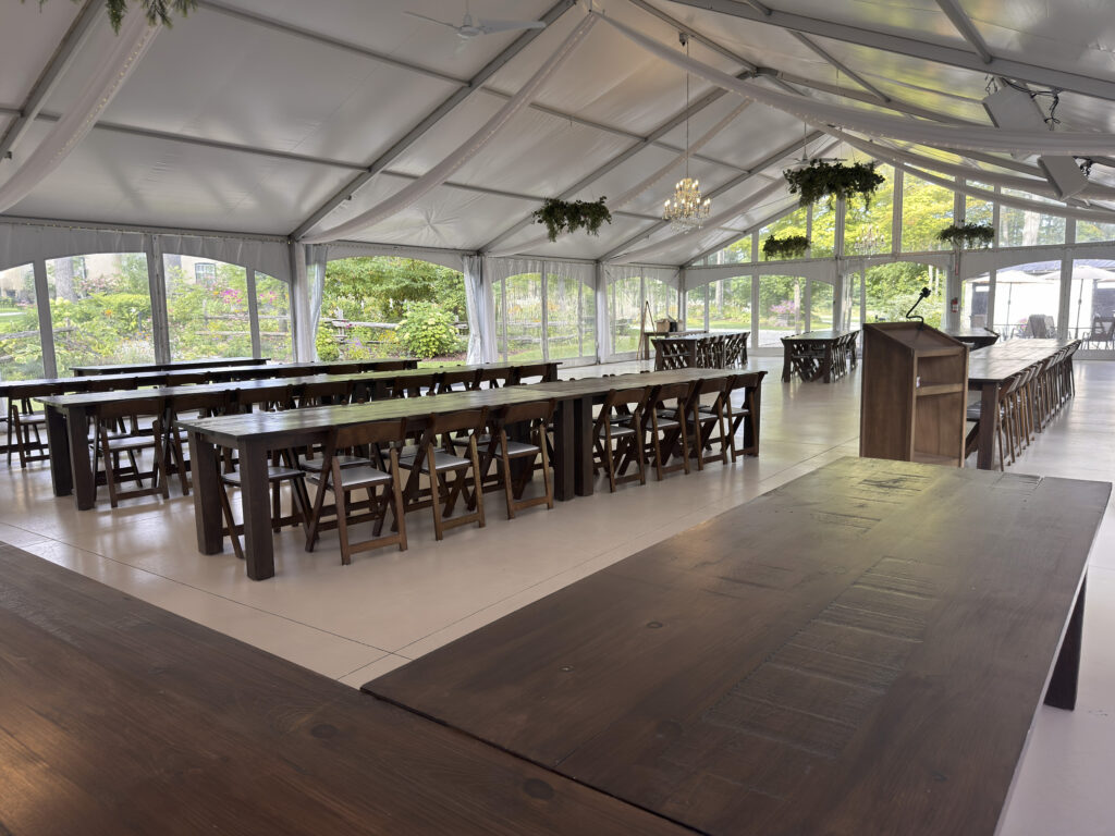 Inside the open-span tent with long harvest tables, hanging plants and a podium