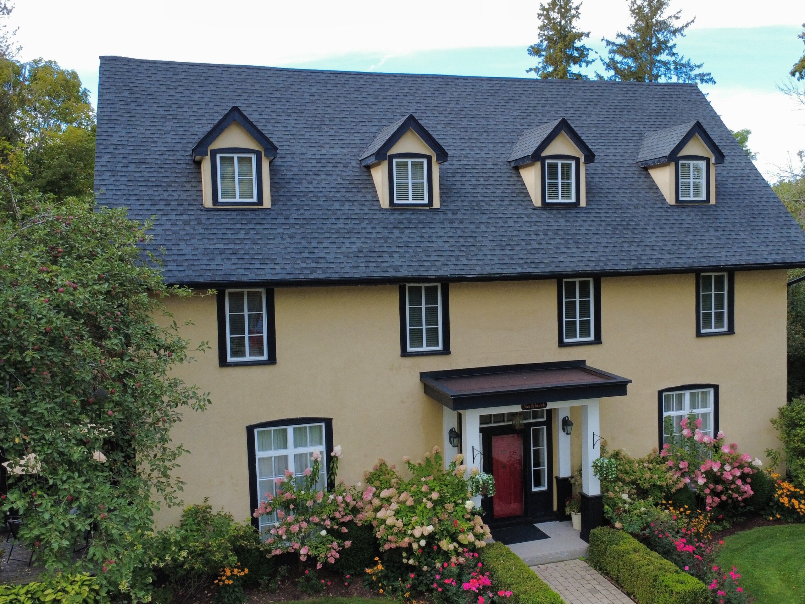 Close view of the 1852 farmhouse's dormer windows and flower-lined entrance at Northbrook Farm near Orillia, Ontario